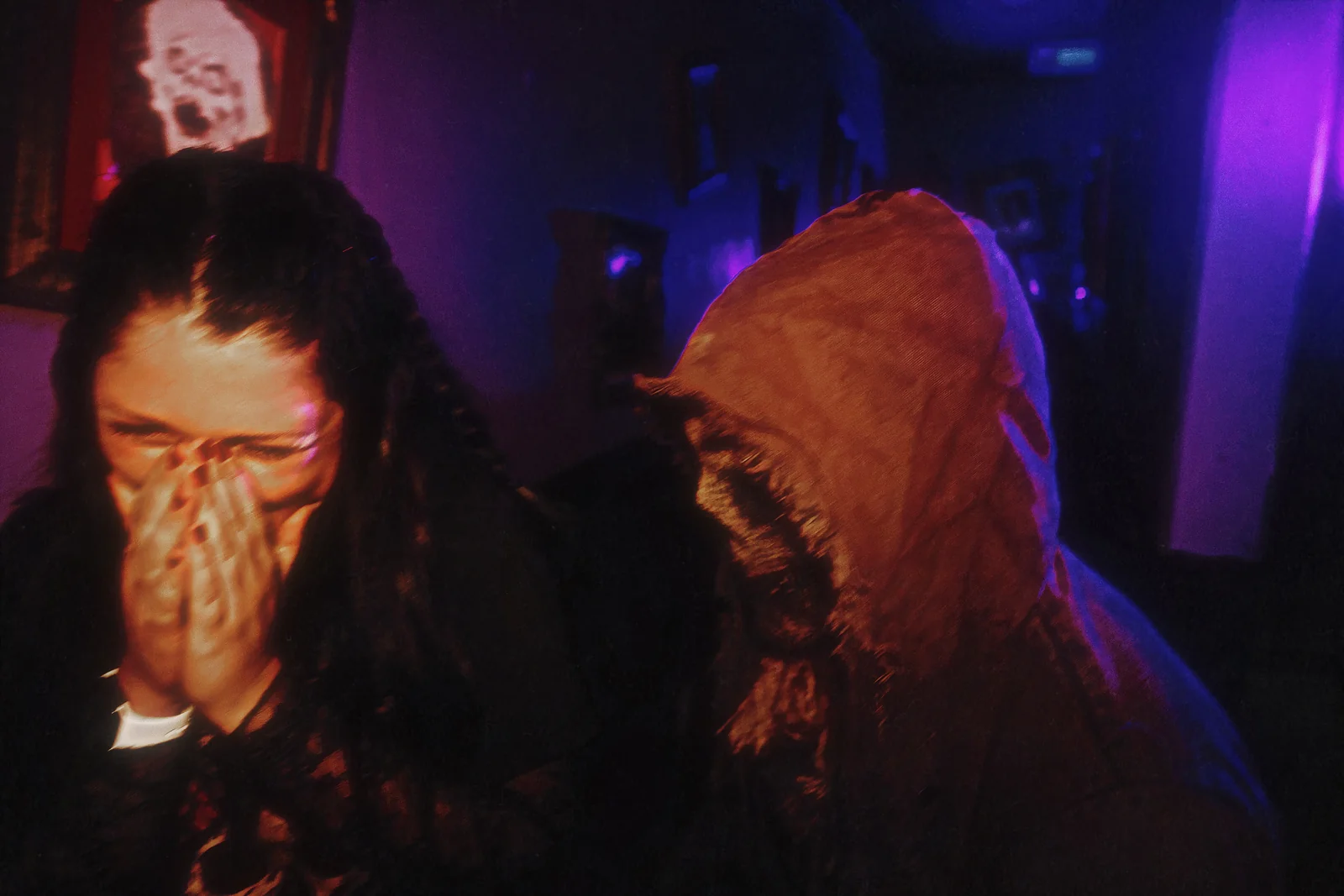 A guest covers her mouth as a hooded character appears beside her.